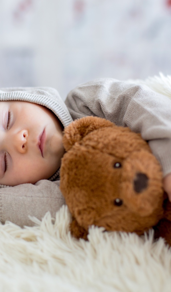 Спящий маленький мальчик обнимает игрушку медвежонка