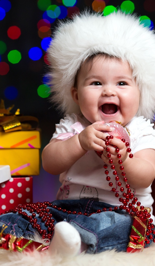 Улыбающийся малыш в новогодней шапке с подарками у елки