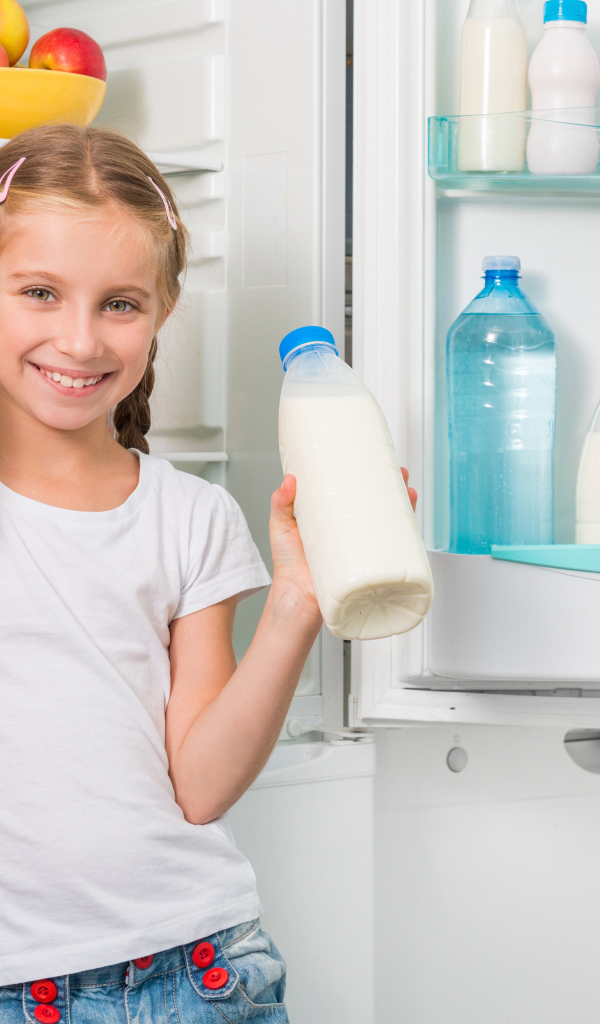 Улыбающаяся девочка у холодильника с сыром и молоком