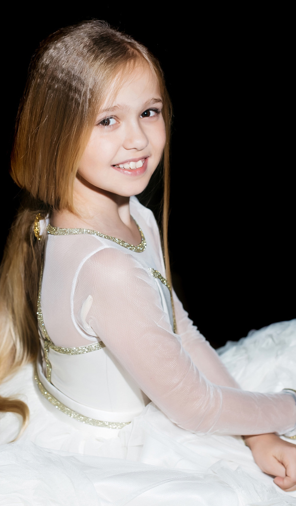 Улыбающаяся девочка в красивом белом платье на черном фоне