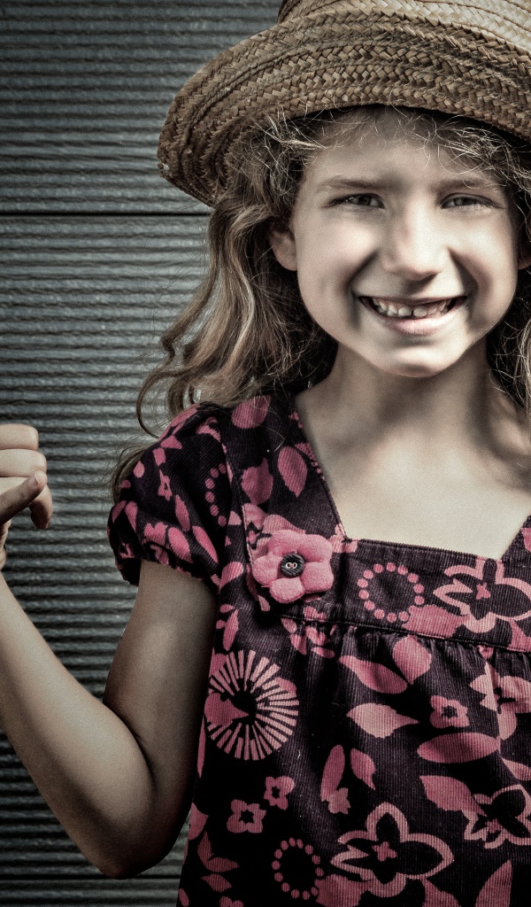 Улыбающаяся девочка в соломенной шляпе у стены 