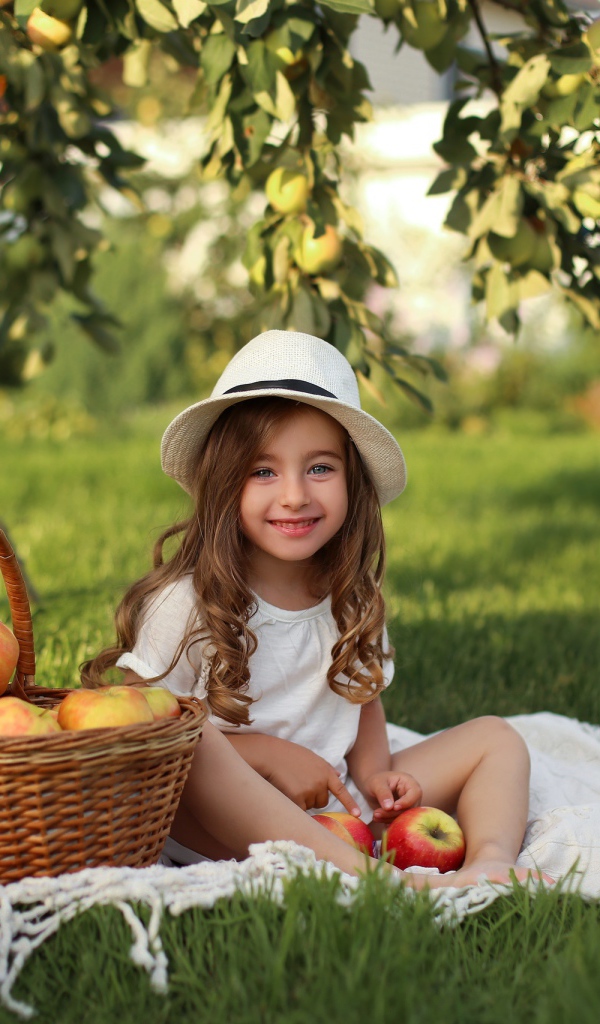 Улыбающаяся девочка сидит на зеленой траве с яблоками