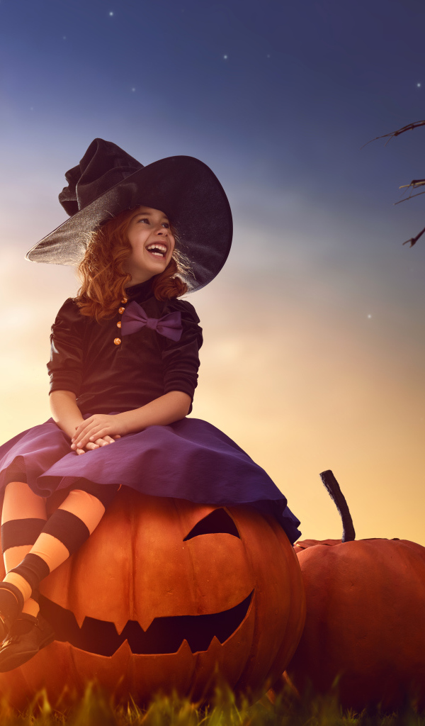 Улыбающаяся девочка сидит на тыкве в костюме на Хэллоуин 