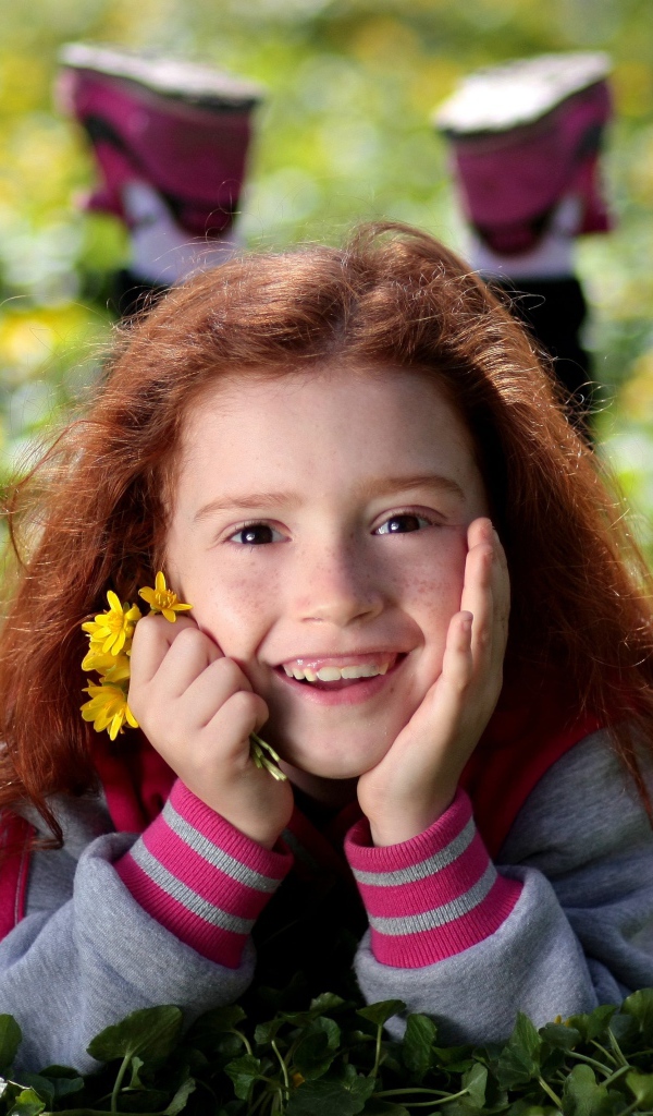 Улыбающаяся рыжеволосая девочка лежит на зеленой траве