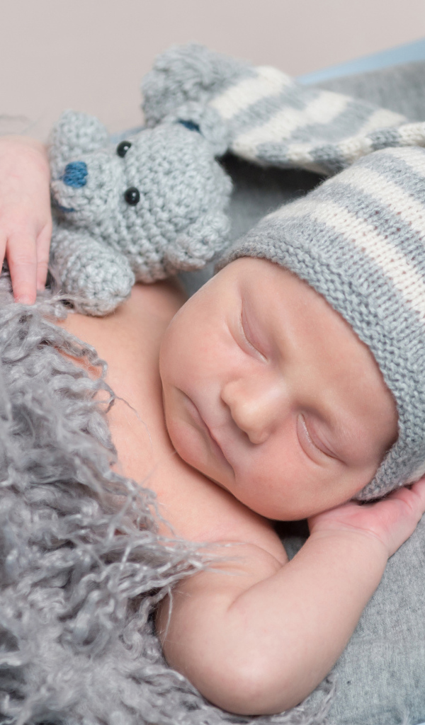 Младенец в вязаной шапке спит с игрушкой под меховым одеялом
