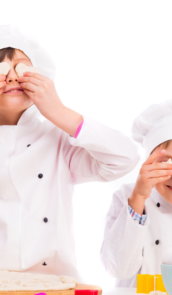 Два маленьких мальчика в костюмах повара на кухне делают печенье