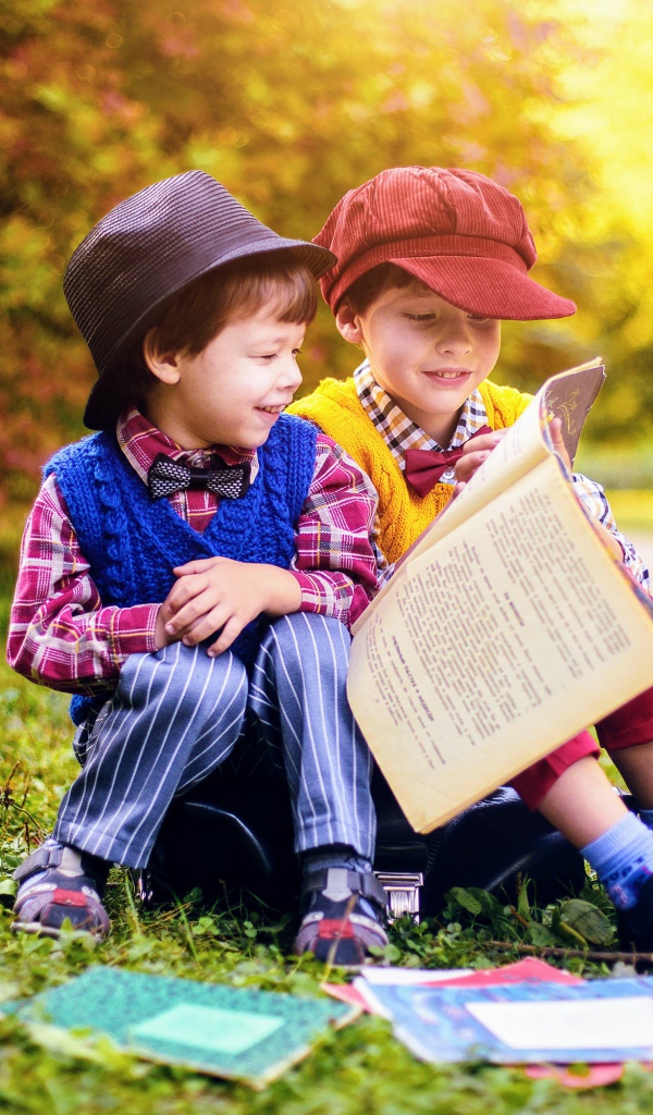 Два маленьких мальчика читают книгу сидя на траве