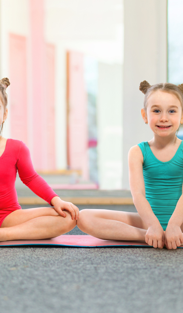 Две маленькие девочки гимнастки сидят на полу