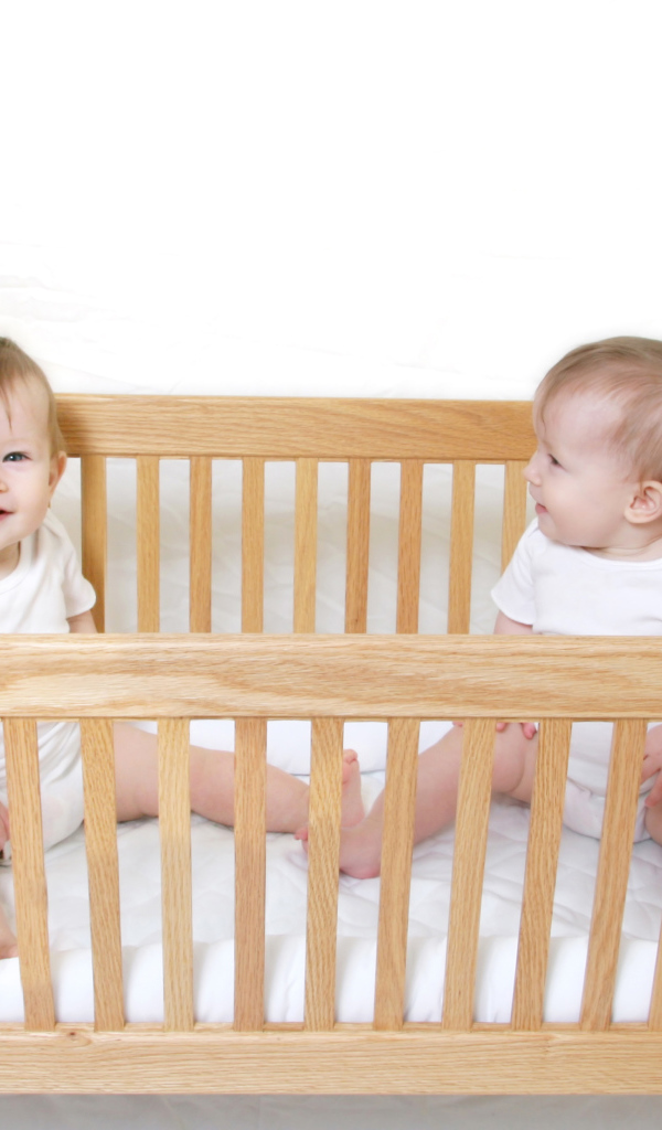 Два улыбающихся малыша в деревянной кроватке