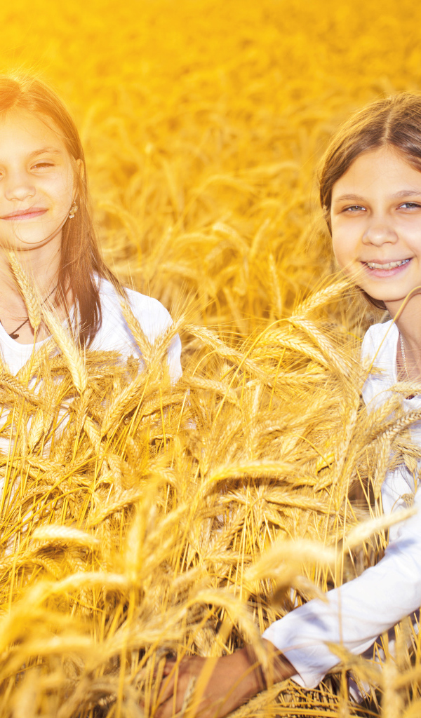 Две улыбающиеся девочки на поле с пшеницей