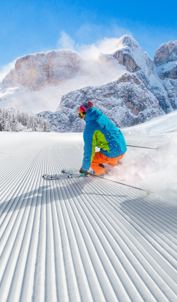 Лыжник спускается по склону на фоне заснеженных гор 