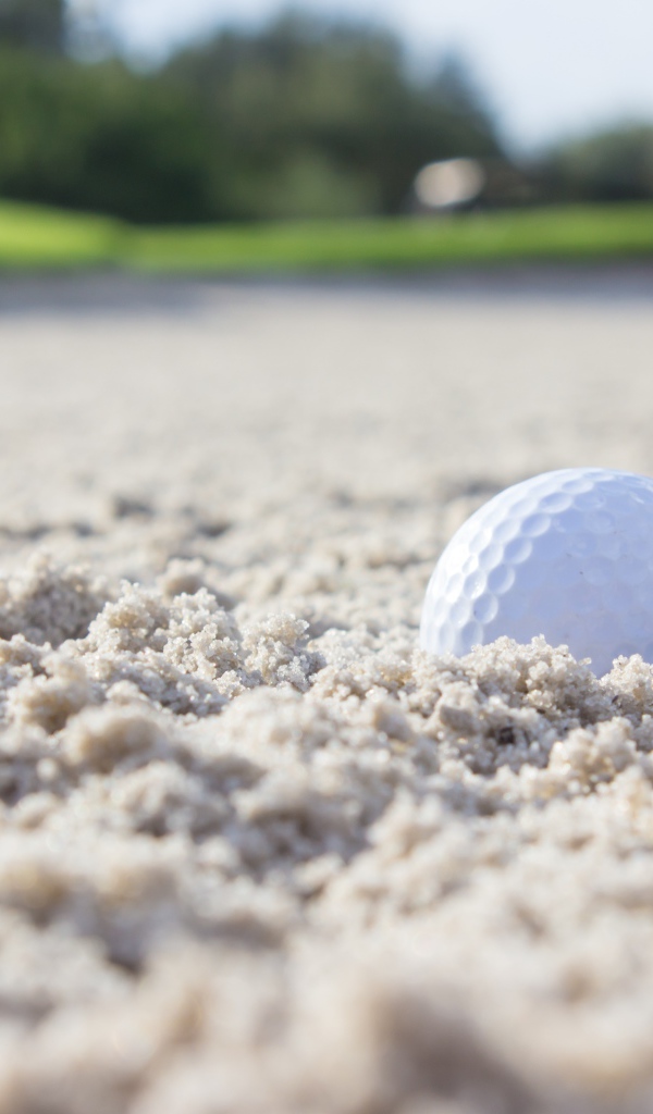 Белый мяч для гольфа лежит на песке