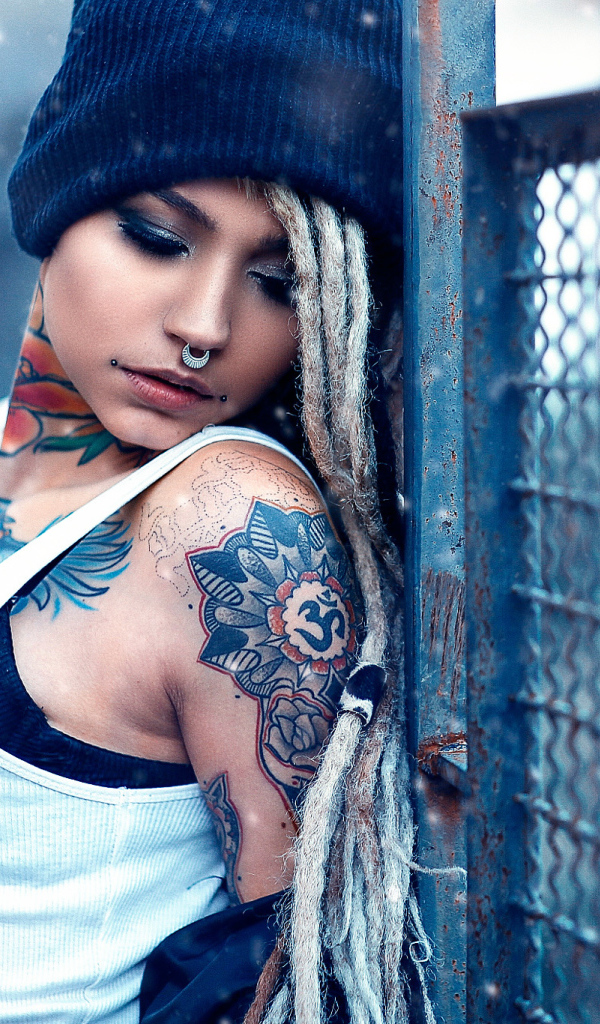 Девушка с татуировками на шее и пирсингом в носу у забора