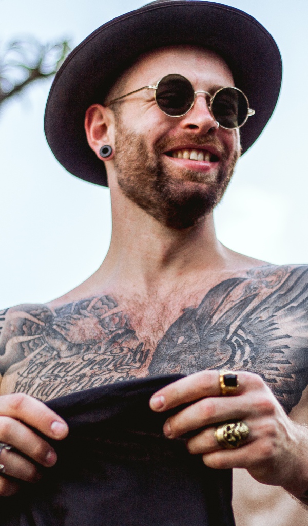 Мужчина с татуировками на теле в черной шляпе и очках