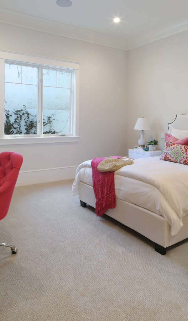 Спальня в светлых тонах с кроватью и столом с красным креслом