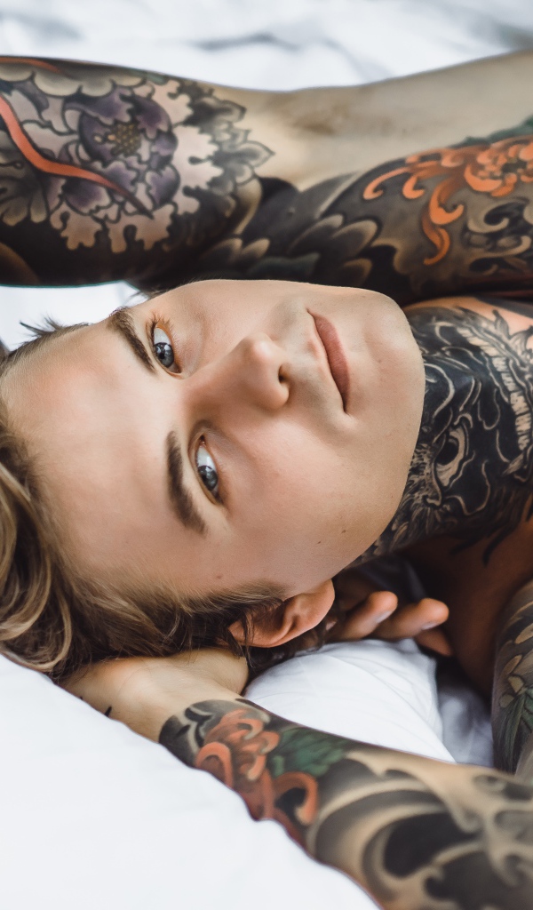 Красивый молодой человек с татуировками на теле лежит на кровати
