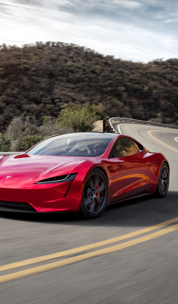 Красный автомобиль Tesla Roadster на трассе у гор 