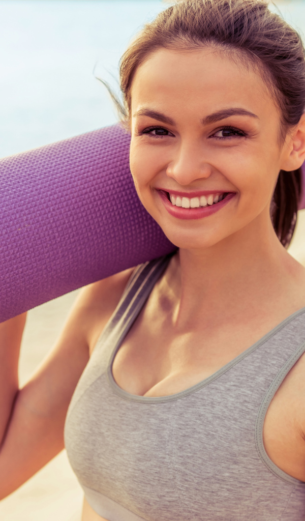 Спортивная девушка с ковриком для йоги на пляже