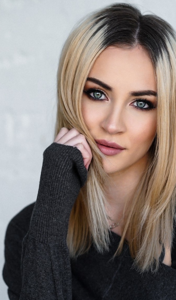 Стильная блондинка с татуировкой на плече на фоне стены