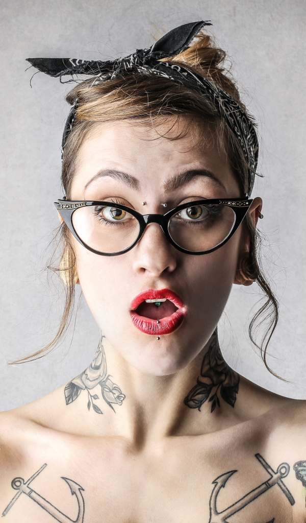 Удивленная девушка в очках с татуировками на теле