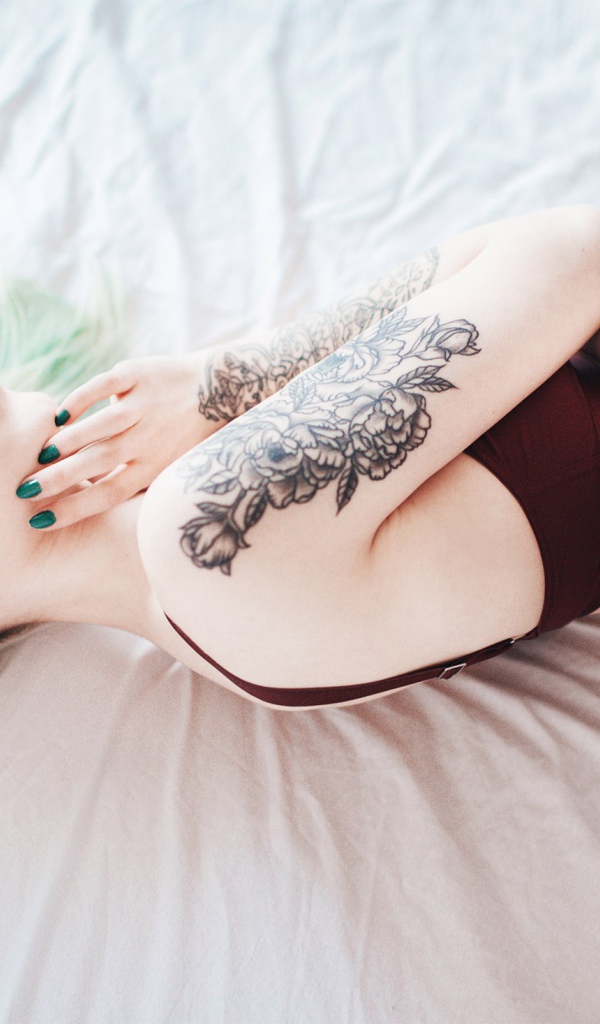 Девушка с татуировкой на руке лежит на кровати 