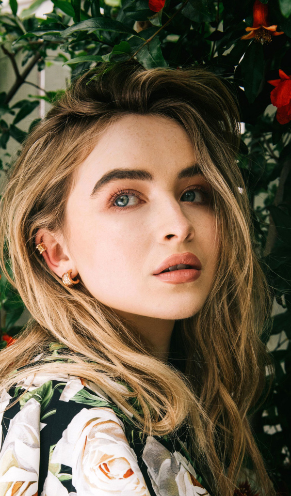 Молодая красивая актриса Сабрина Карпентер у красных цветов