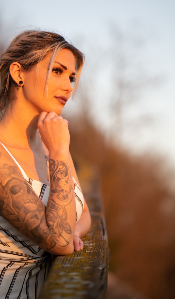 Молодая девушка с татуировкой на руке в лучах солнца
