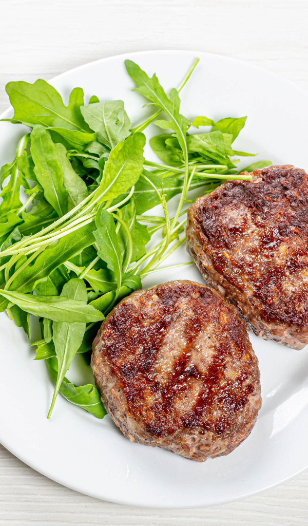 Две котлеты на тарелке с зеленью рукколы 