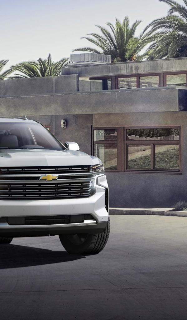 Серый внедорожник Chevrolet Suburban, 2021 года на фоне дома