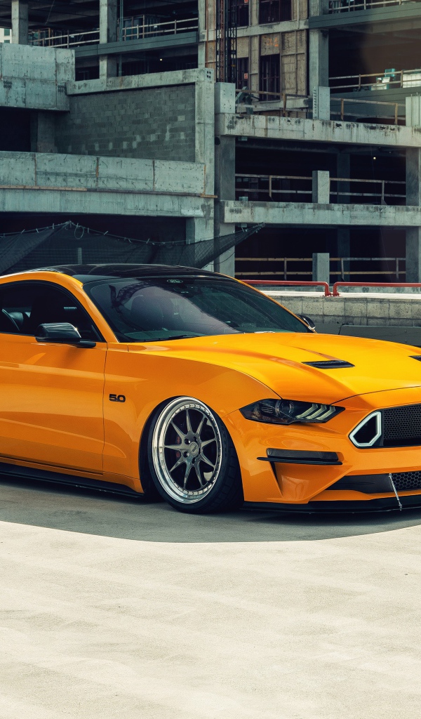 Оранжевый автомобиль Mustang у заброшенного здания 