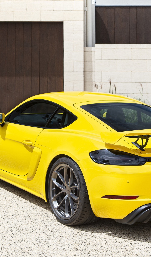 Желтый автомобиль Porsche 718 Cayman GT4, 2020 года у гаража 