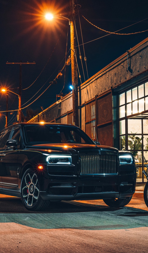 Черный стильный автомобиль Rolls-Royce Cullinan на улице города с байкерами