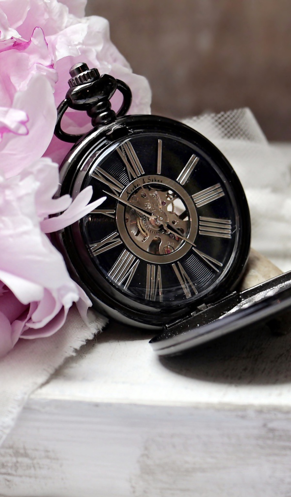 Черные карманные часы с книгой и цветами на столе 