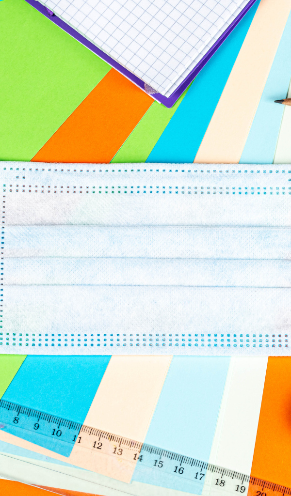 Маска от коронавируса лежит на цветной бумаге с канцелярскими предметами