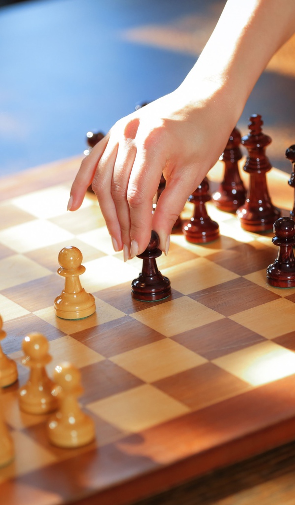 Женская рука переставляет шахматы на доске 
