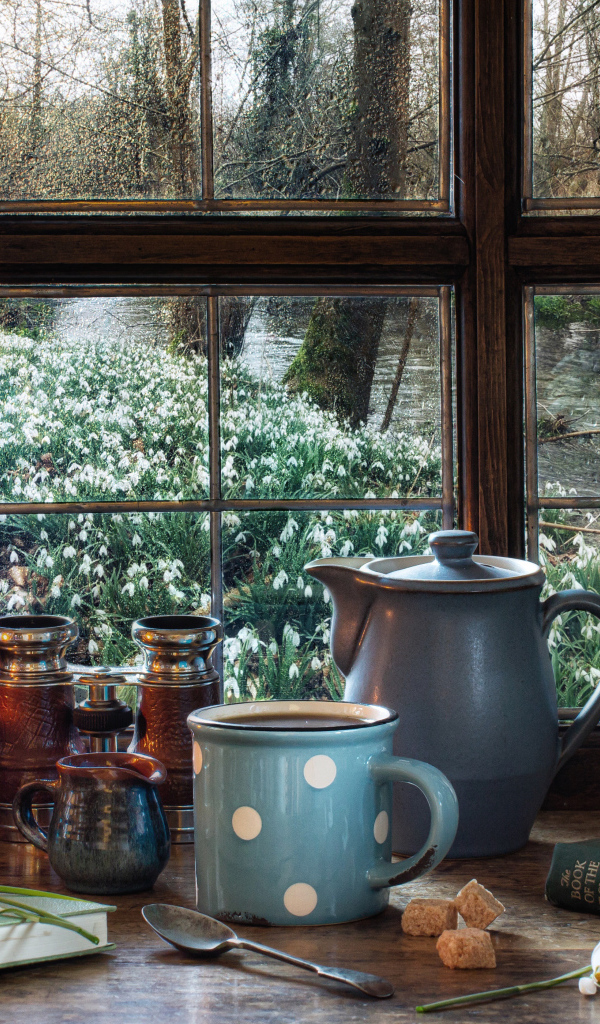 Керосиновая лампа на столе с кружкой, книгами и букетом подснежников у окна