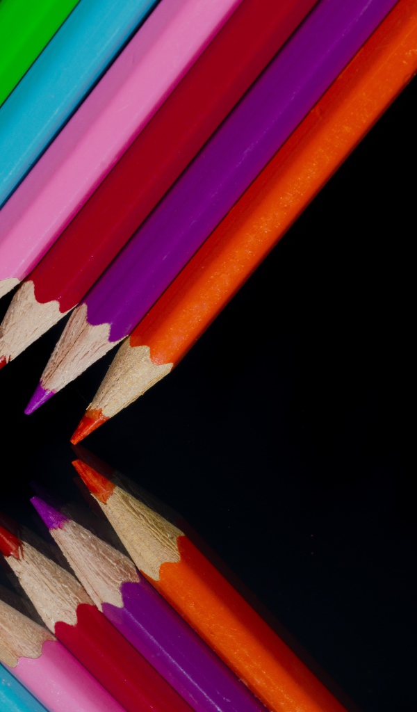 Разноцветные карандаши отражаются в черной зеркальной поверхности 