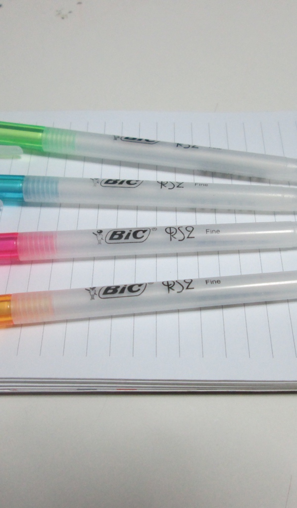 Разноцветные ручки лежат на блокноте на белом фоне 