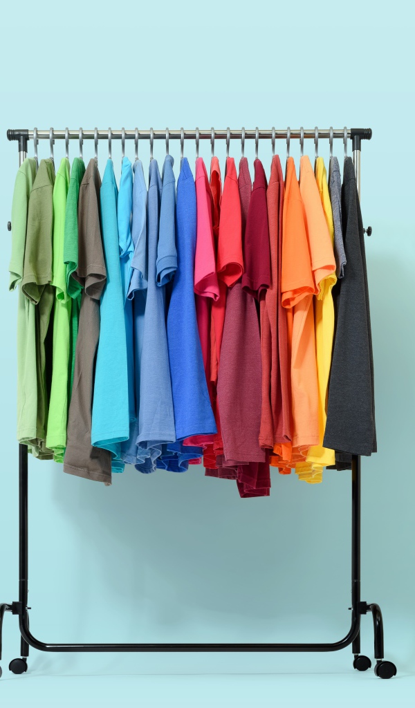 Разноцветные футболки на вешалке на голубом фоне