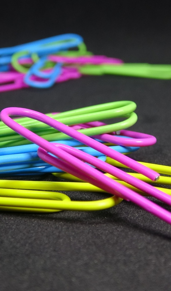 Разноцветные скрепки на черном столе 