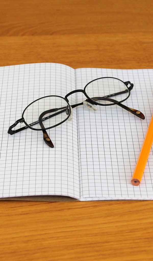Тетрадь, ручка, карандаш и очки лежат на парте