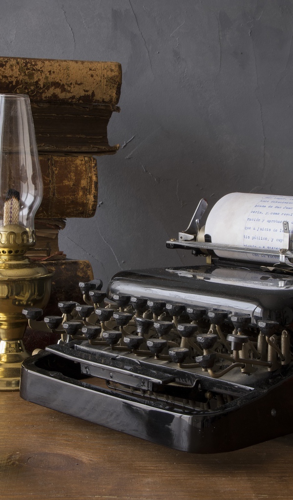 Старая печатная машинка, книги, керосиновая лампа и трубка на столе 