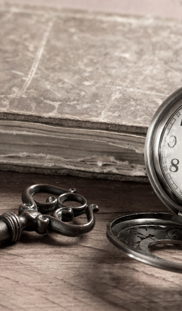 Карманные часы на столе с ключом и старой книгой 