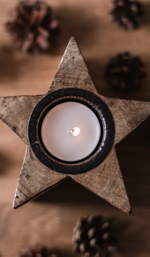Свеча в форме звезды на столе с шишками и сушеным апельсином