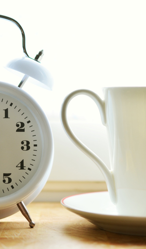 Белый будильник и чашка кофе на утреннем столе
