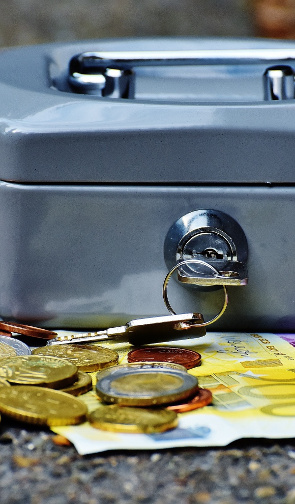 Монеты и купюры на столе с маленьким сейфом