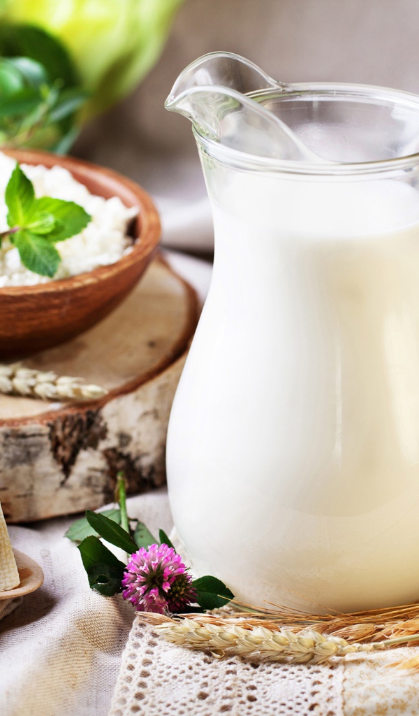 Кувшин с молоком стоит на столе с сыром и творогом