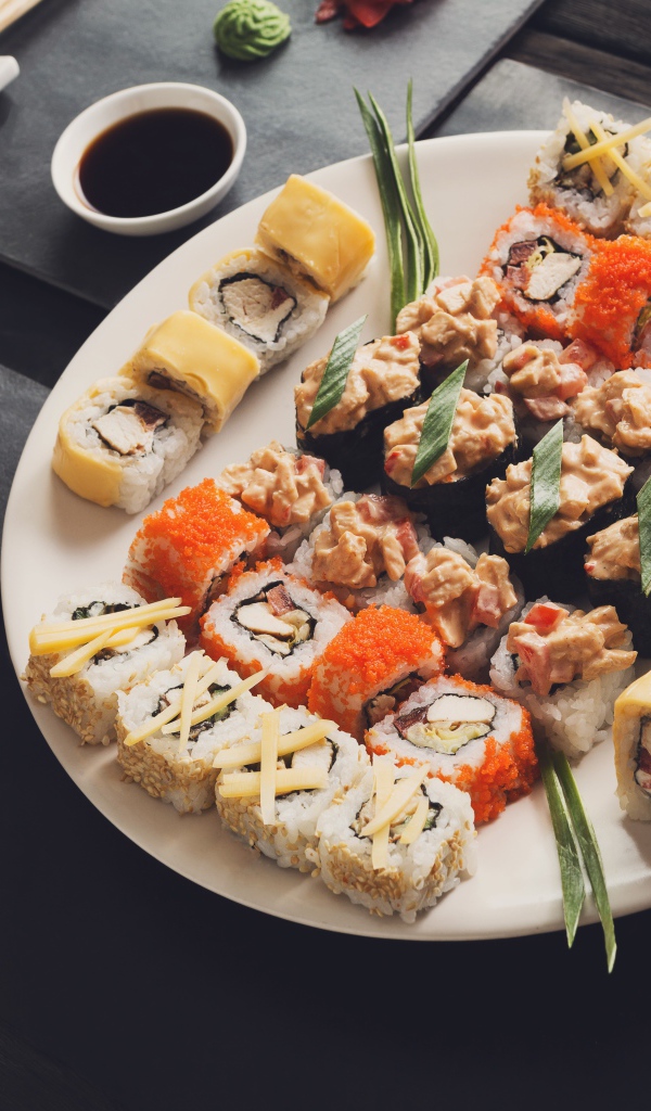 Аппетитные роллы на большой тарелке на столе с соусом