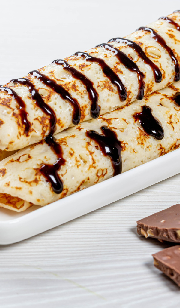 Аппетитные тонкие блины на белой тарелке с шоколадом