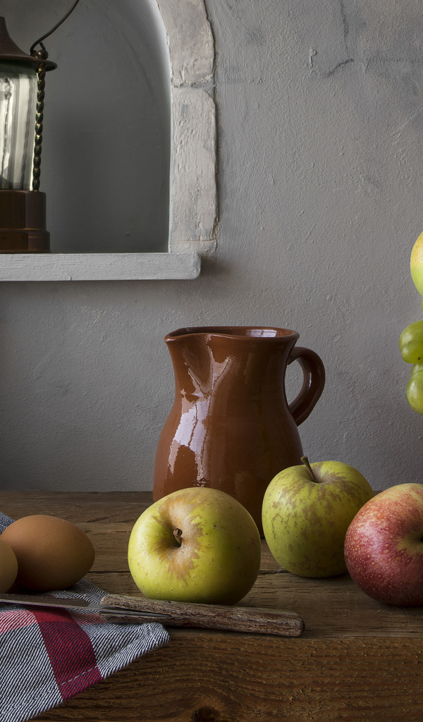 Корзина с яблоками и виноградом на столе с хлебом и яйцами